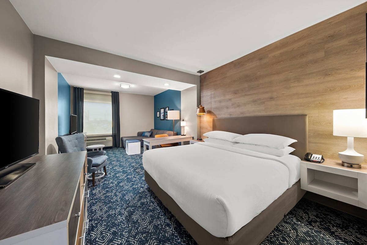 A hotel room with a large bed, a desk with a chair, a TV, and a lamp.