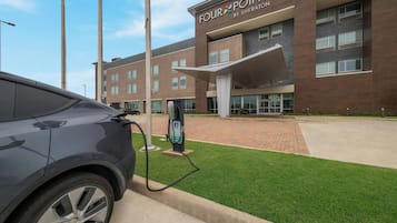 A modern building with a sign reading 'FOUR POINTS BY SHERATON' and an electric vehicle charging station in front.