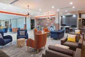 A modern lounge area with sofas, armchairs, and a flat-screen TV. - Four Points by Sheraton Plano (Plano)