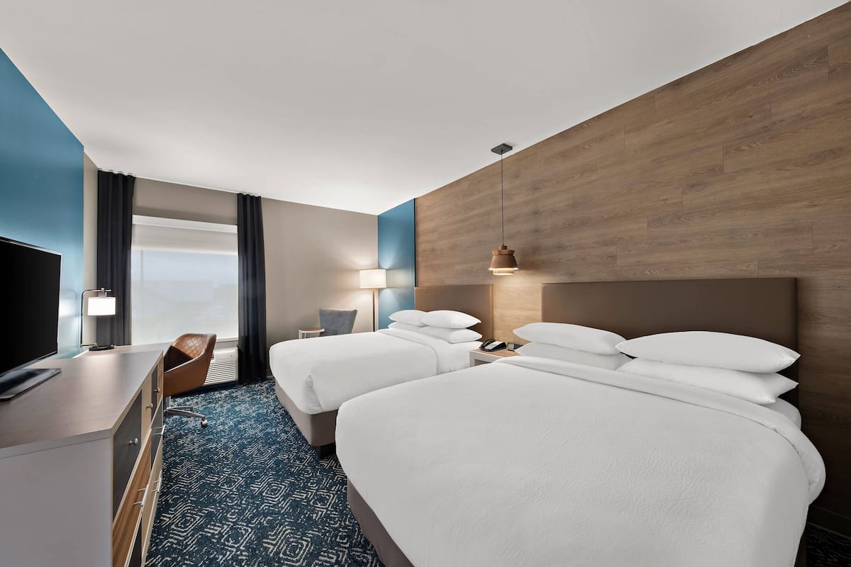 A hotel room with two beds, a desk, and a chair.