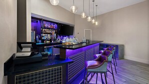 Una zona de bar con mostrador, taburetes, televisor y una variedad de botellas y vasos.