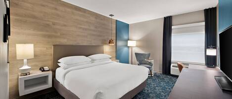 A hotel room with a large bed, bedside lamps, a desk, and a view of the outdoors.