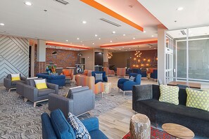 A modern lounge area with sofas, armchairs, and a coffee table, featuring a brick wall and a large window. - Four Points by Sheraton Plano (Plano)
