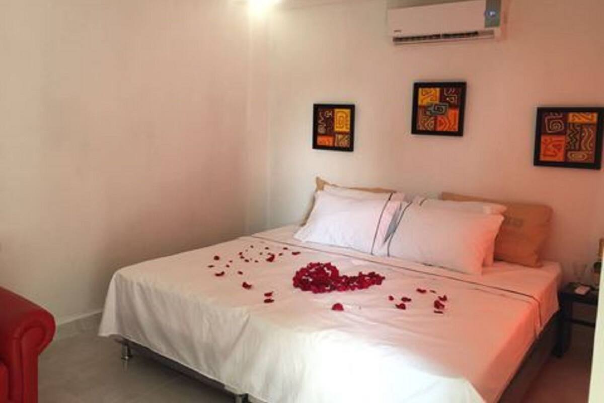 Quarto de hotel com uma cama, mesa de cabeceira e uma cadeira vermelha.