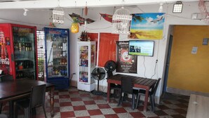 A restaurant interior with a checkered floor, a Coca-Cola refrigerator, a Postobon refrigerator, a fan, and a menu board. - Manzanillo Beach (Cartagena)