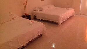 A hotel room with two single beds, a small table with a vase of flowers, and a wall-mounted artwork. - Manzanillo Beach (Cartagena)