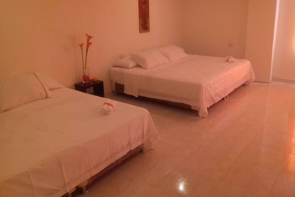 Quarto de hotel com duas camas de solteiro, uma mesinha com um vaso de flores e uma obra de arte na parede.