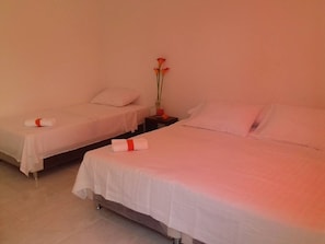 A hotel room with two beds, each with white linens and a red ribbon. There is a vase with flowers on a nightstand between the beds. - Manzanillo Beach (Cartagena)