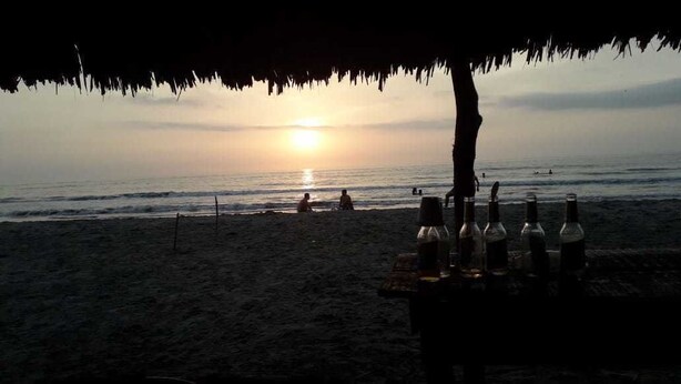 A beach scene with a sunset, bottles on a table, and people in the background. - Manzanillo Beach (Cartagena)