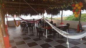 A patio area with tables and chairs, a hammock, and a view of the ocean. - Manzanillo Beach (Cartagena)