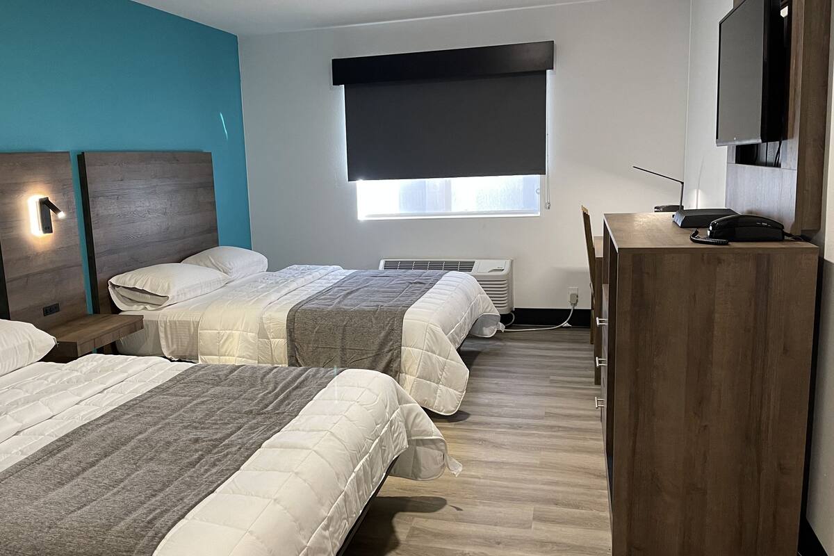 Ein Hotelzimmer mit zwei Betten, einem Schreibtisch, einem Fernseher und einem Fenster mit Jalousie.