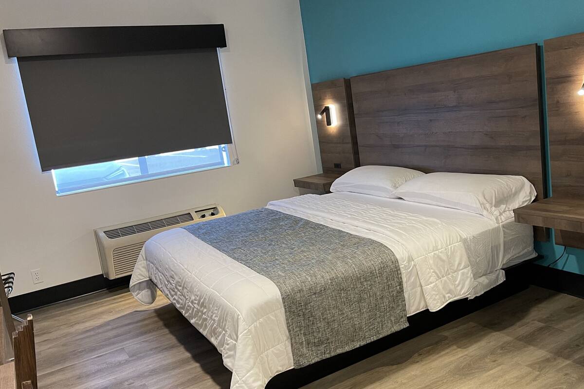 Ein modernes Schlafzimmer mit Bett, Fenster mit Jalousie, Wandleuchte und Nachttisch.