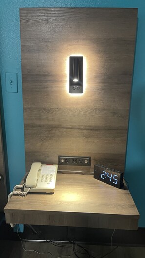 Ein Holztisch mit einer Wandleuchte, einem Telefon und einer digitalen Uhr, die 2:45 Uhr anzeigt.