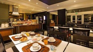 Un comedor de hotel con mesas preparadas para el desayuno, una estación de café y una zona de bufé.