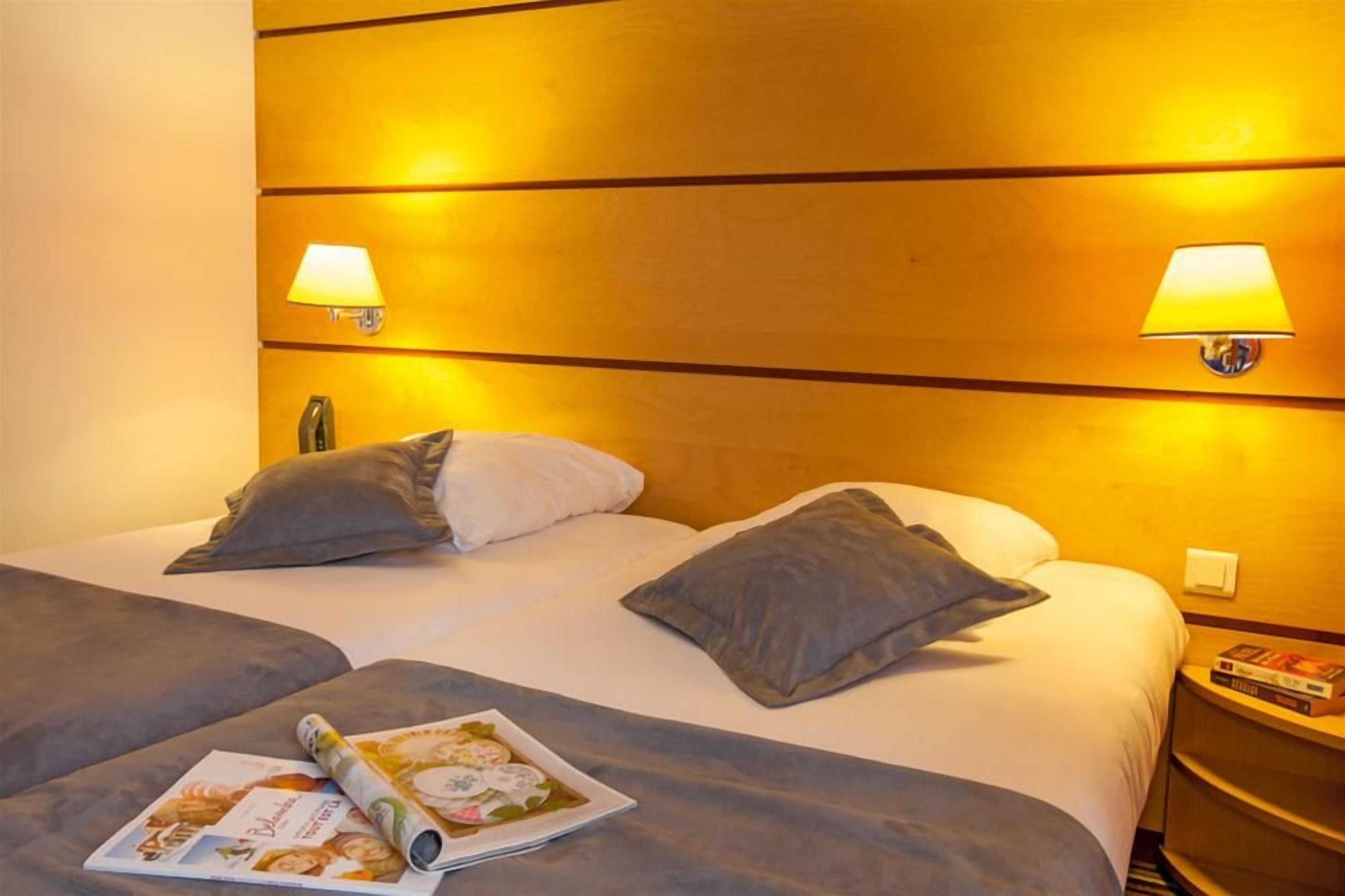 Una habitación de hotel con una cama grande, dos lámparas de noche y una mesita de noche con un libro.