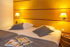 A hotel room with a large bed, two bedside lamps, and a nightstand with a book. - Le Magendie (Paris)