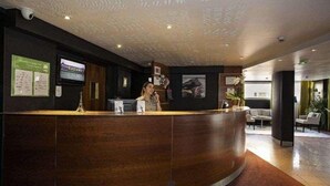 Una recepción con una recepcionista detrás, un televisor en la pared y un techo con diseño ornamental.