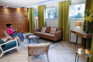 A modern living room with a brown sofa, a wicker chair, a teal armchair, and a small round table. - Le Magendie (Paris)