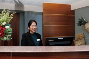A reception desk with a Lenovo computer, a name tag, and a plant with red flowers. - Le Magendie (Paris)