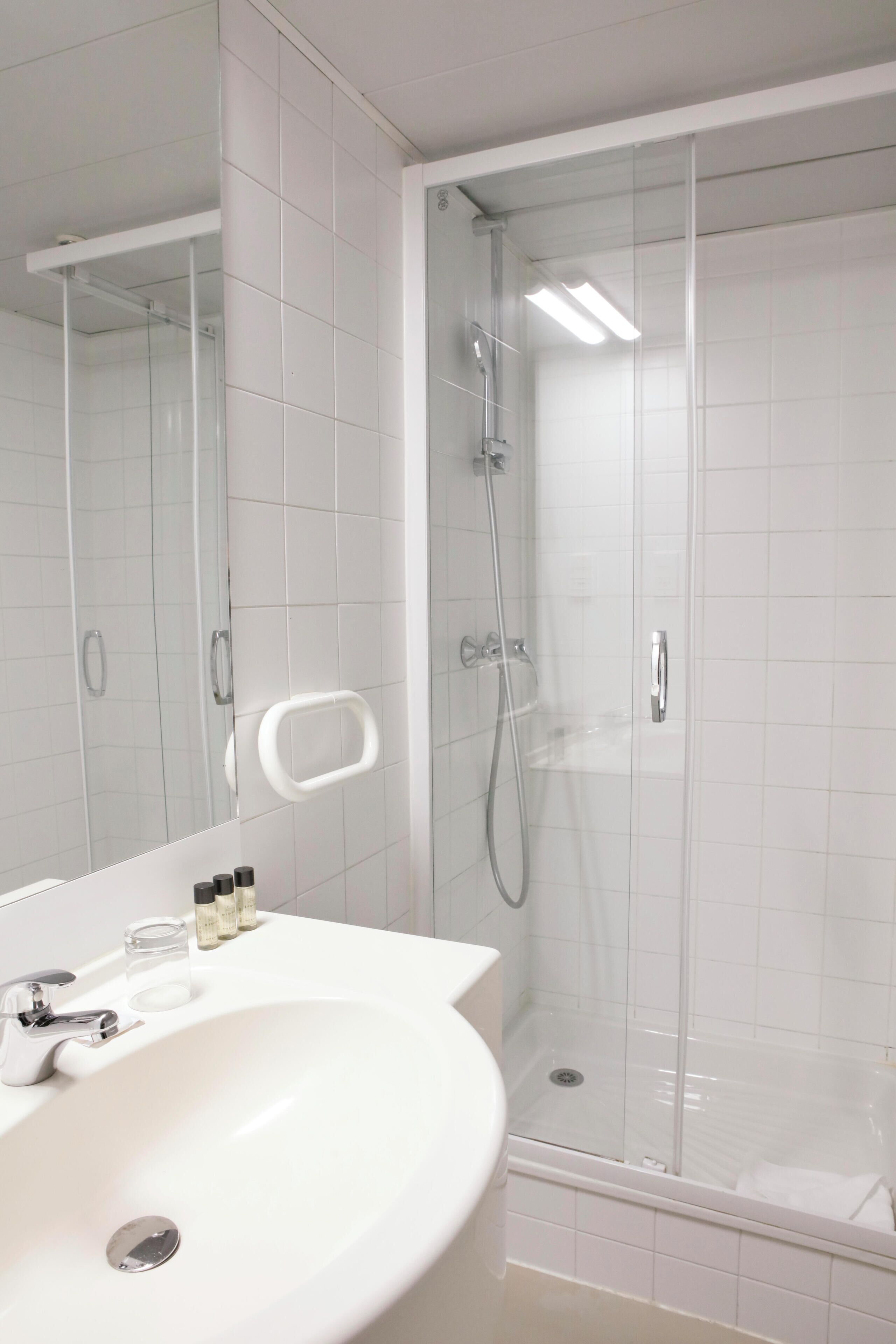 Ein modernes Badezimmer mit einem weißen Waschbecken, Spiegel und einer Duschkabine aus Glas.