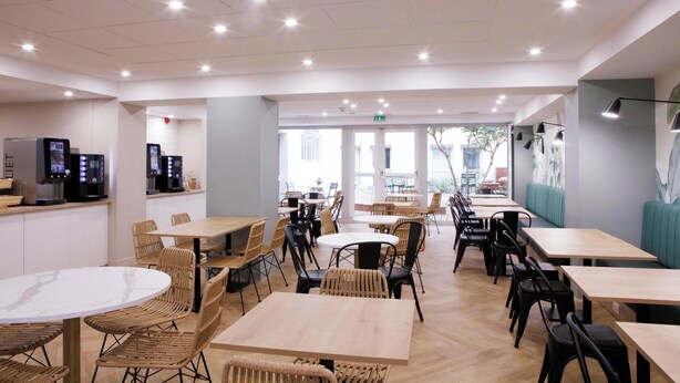 A modern restaurant with multiple seating areas, including round tables and booths, and a counter with digital menu displays. - Le Magendie (Paris)