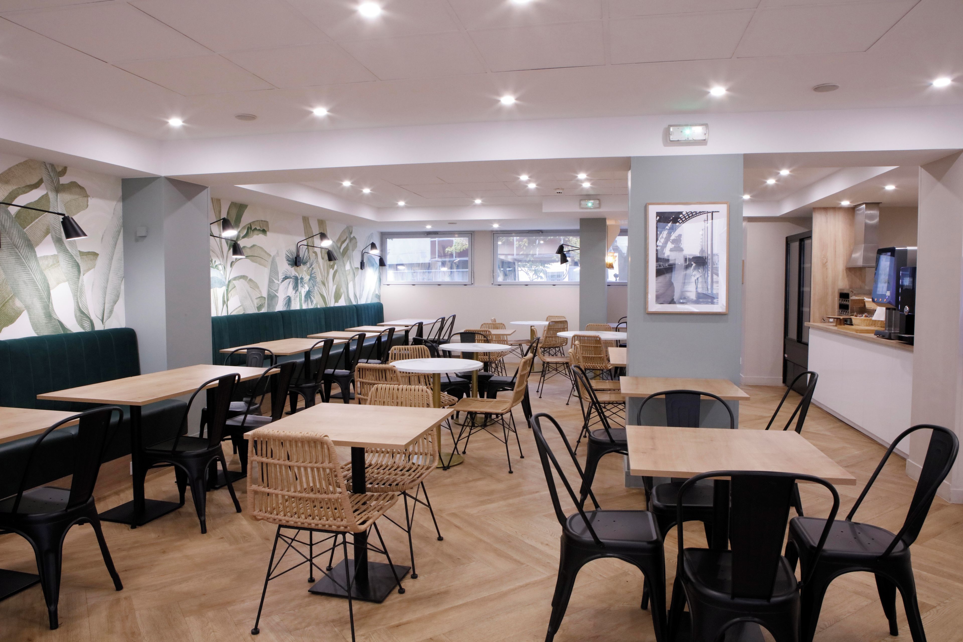 Ein modernes Restaurantambiente mit Holztischen und -stühlen, einer grünen Sitzgruppe mit Polsterbänken und großen Fenstern für natürliches Licht.