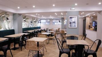 Ein modernes Restaurantambiente mit Holztischen und -stühlen, einer grünen Sitzgruppe mit Polsterbänken und großen Fenstern für natürliches Licht.