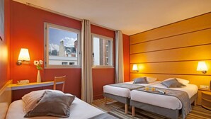 Habitación de hotel con dos camas, un escritorio y una ventana con cortinas.