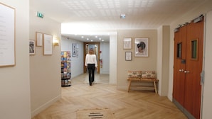 A hallway with wooden flooring, framed artwork on the walls, a bench, and a wooden door. - Le Magendie (Paris)