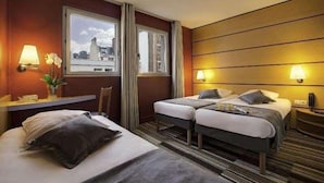 A hotel room with two beds, a desk, and a window with a city view. - Le Magendie (Paris)