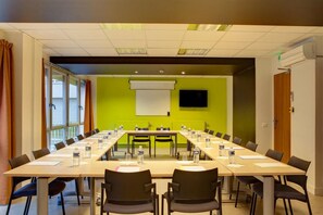 A conference room with a long table, chairs, a projector screen, and a television on the wall. - Le Magendie (Paris)