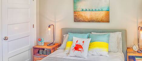 Een keurig opgemaakt slaapkamer met een bed, nachtkastje, lamp en een schilderij aan de muur.