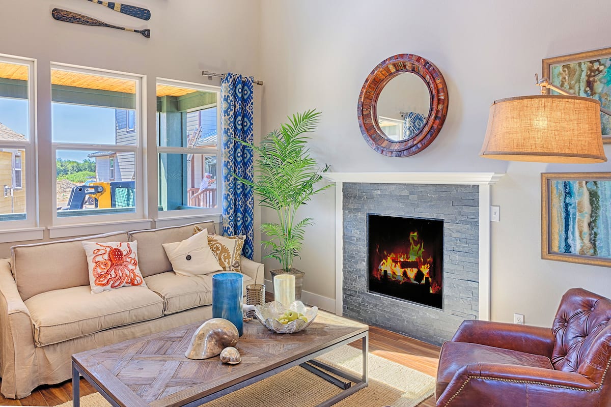 Una sala de estar con un sofá color beige, un sillón de cuero marrón, una mesa de centro, una chimenea y un ventanal con cortinas.