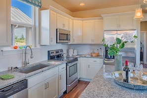 A modern kitchen with white cabinets, stainless steel appliances, a granite countertop, and a view of the outdoors. - Oyhut Bay Resort (Ocean Shores)