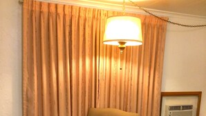 A room with a single wooden chair, beige curtains, a hanging lamp, and an air conditioning unit on the wall.