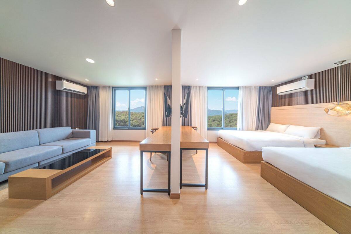 A modern hotel room with a large bed, a sofa, a dining table, and a view of the mountains through large windows.