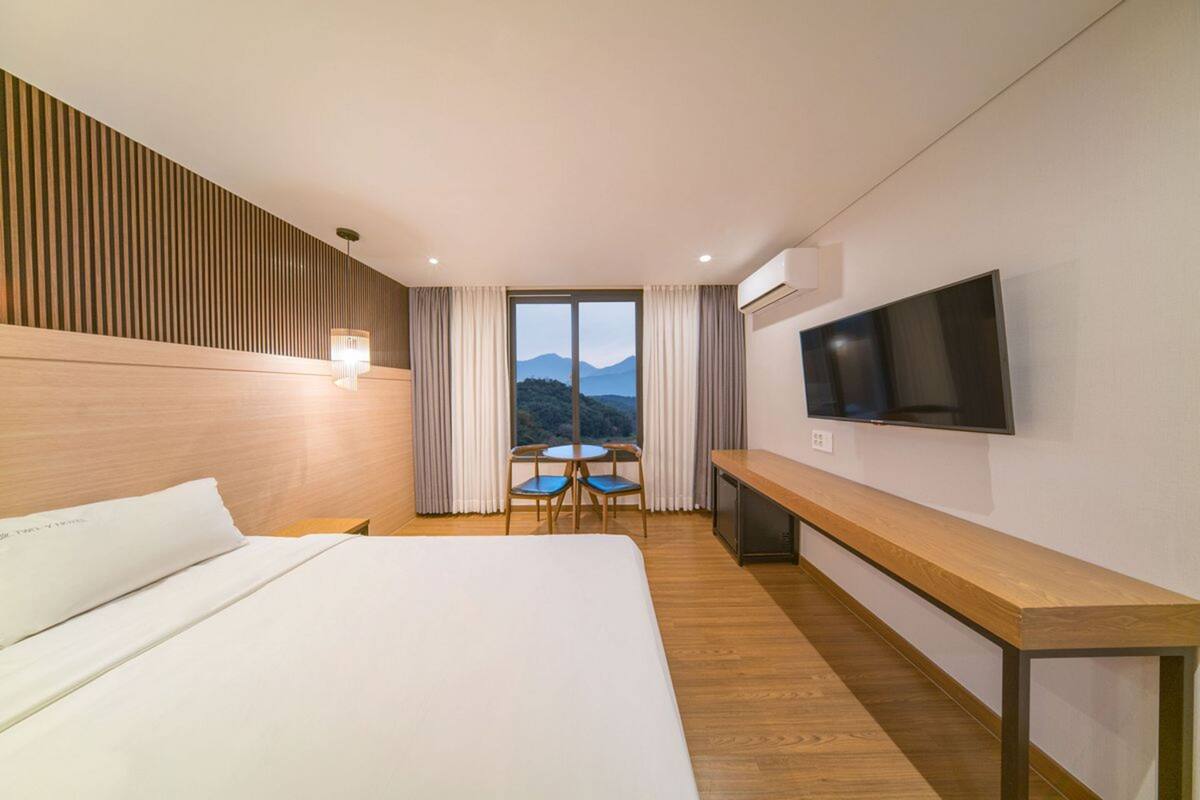 A hotel room with a large bed, a TV mounted on the wall, a wooden bench, and a table with chairs.