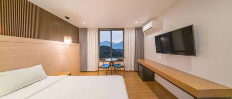 Une chambre d’hôtel avec un grand lit, un téléviseur fixé au mur, un banc en bois et une table avec des chaises.