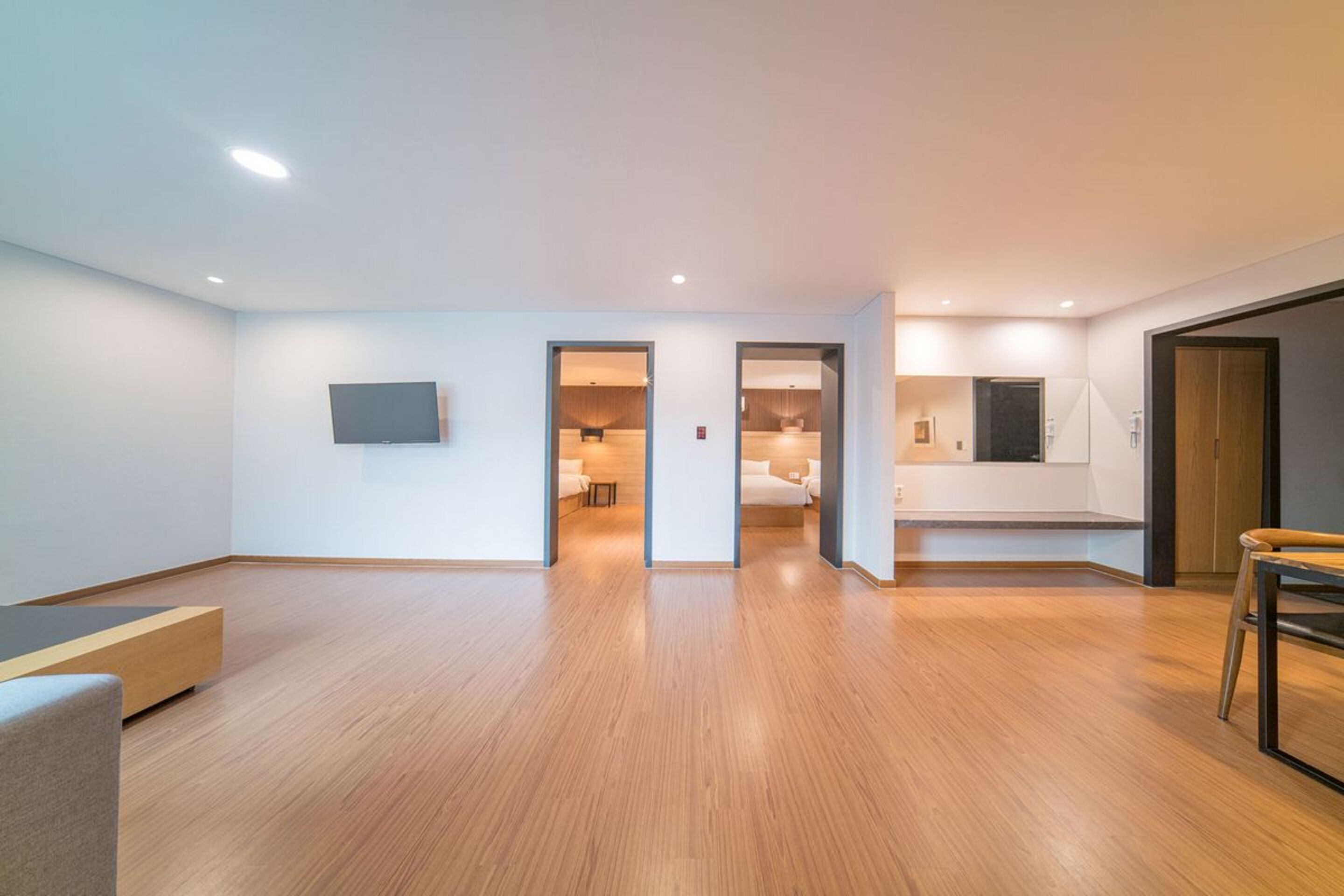 A modern, open-plan living space with a wooden floor, a flat-screen TV mounted on the wall, and a dining area with a table and chairs.