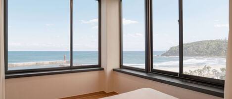 A bedroom with a large window offering a view of the ocean and a distant coastline.