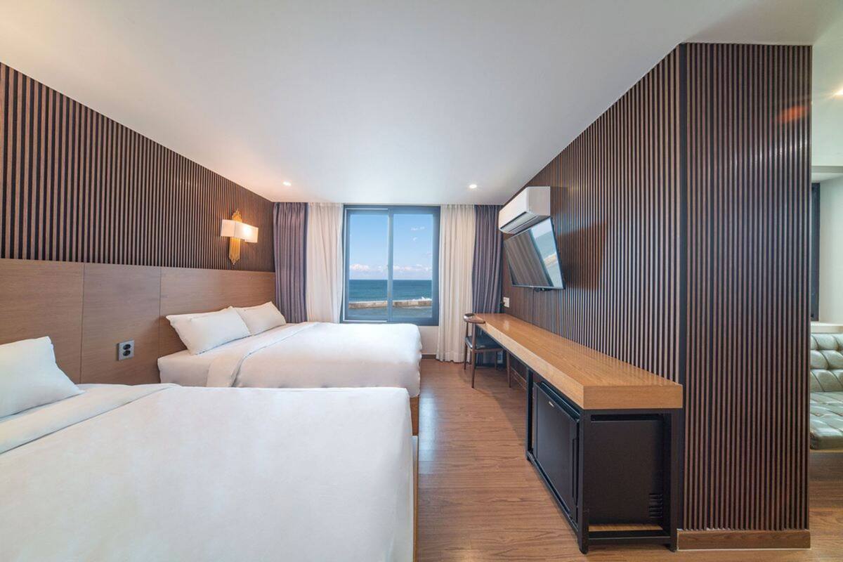 A hotel room with two beds, a wooden desk, a TV, and a large window with a view.