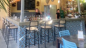 An indoor bar area with a counter, seating, hanging pendant lights, a menu board, and a refrigerator.