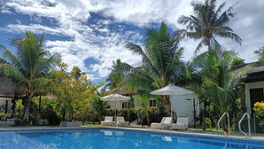 A swimming pool with tiled edges, surrounded by palm trees and lounge chairs.