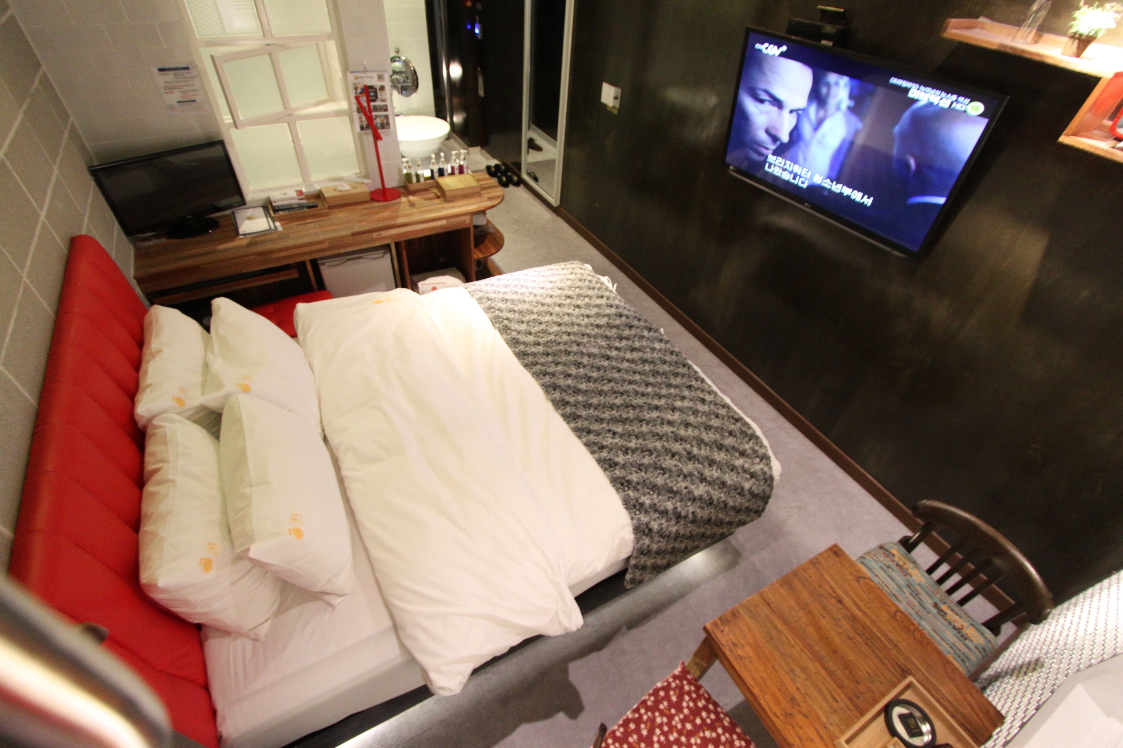 A hotel room with a bed, a small table, a TV, and a window.
