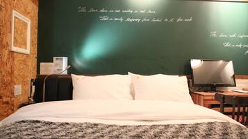 A neatly made bed with white linens and a gray blanket, a television on a wooden table, and a chalkboard wall with writing.