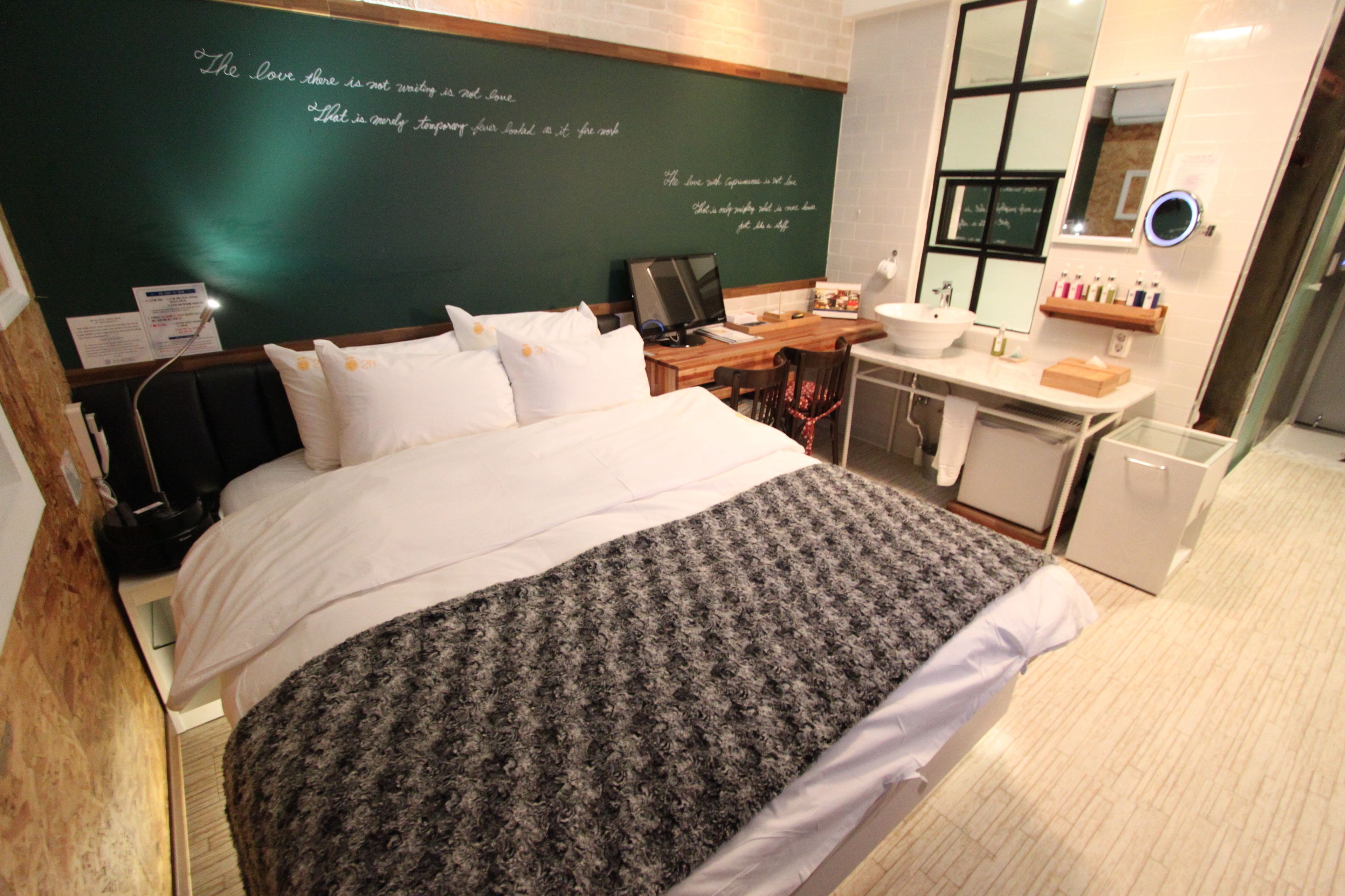 A hotel room with a bed, a desk, a computer, a sink, and a mirror.