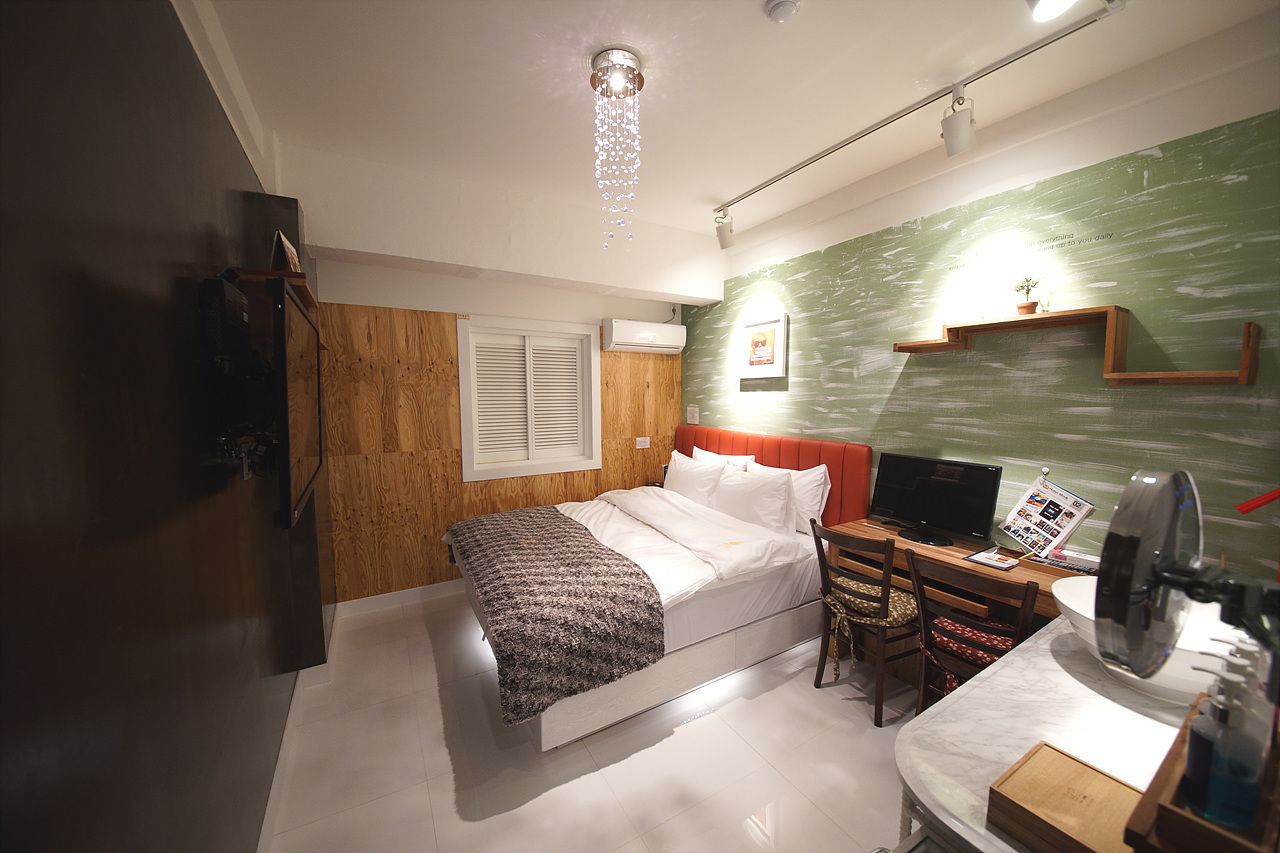 Un dormitorio con cama, escritorio con computadora, silla, espejo y repisa en la pared con una planta.