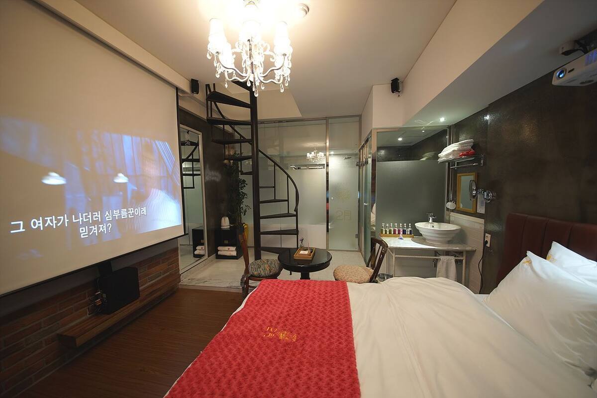 Ein Hotelzimmer mit Bett, Fernseher, einer Kristallleuchtre, einem Badezimmer und einer Treppe.