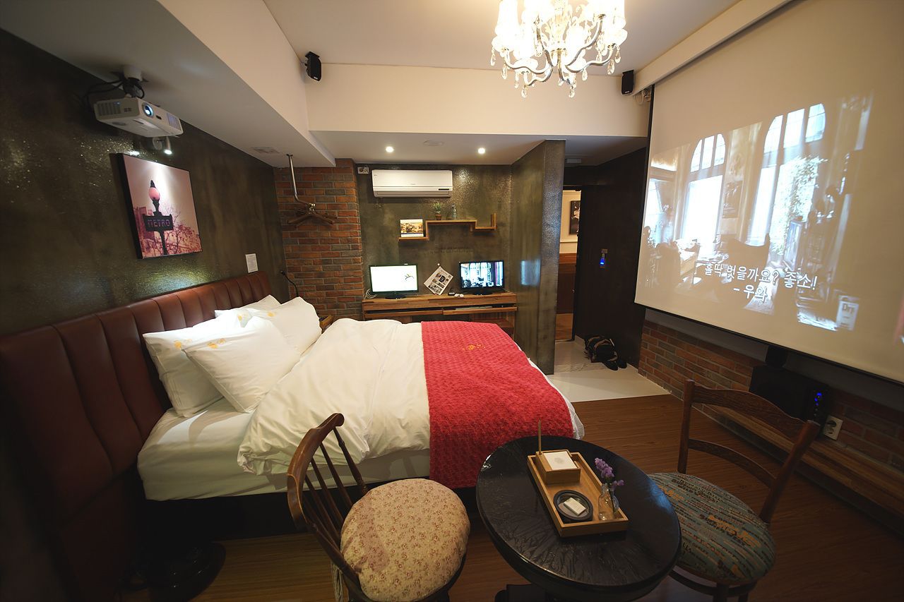Ein Hotelzimmer mit einem Bett, einem Schreibtisch mit Computer, einer Projektionsleinwand und einer Chandelier.