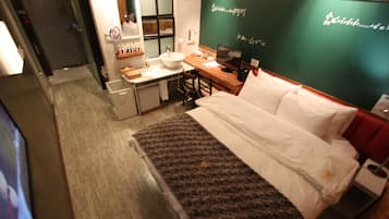 A hotel room with a bed, a desk with a computer, a sink, and a mirror.
